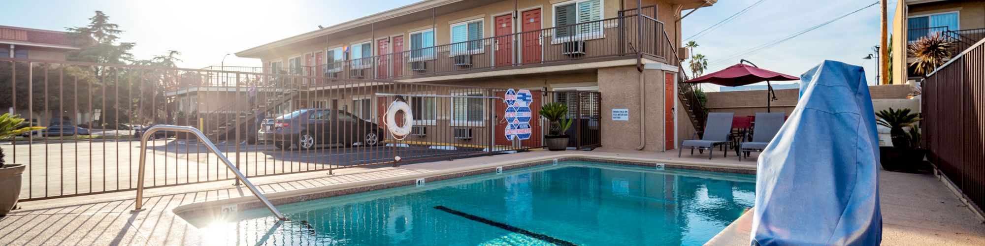 An outdoor swimming pool with a railing, poolside furniture, and a two-story building in the background under a bright blue sky, ends the sentence.