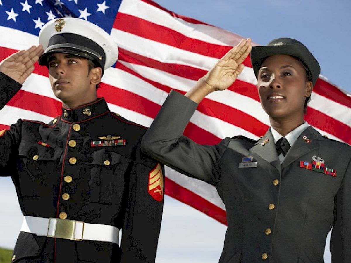 Two military personnel are saluting in front of an American flag.