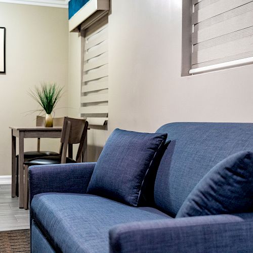 The image shows a room with a blue sofa, a table with a chair, a small plant, and a framed picture on the wall.