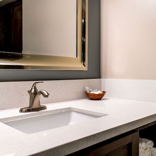 A bathroom sink with a modern faucet, a large mirror above, and a small decorative bowl on the counter. Towels are visible in the cabinet below.