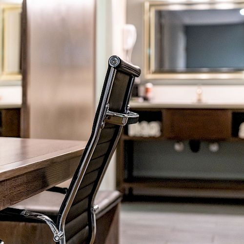 The image shows a modern office space with a black office chair and wooden desk, a counter with shelves, and a mirror in the background.