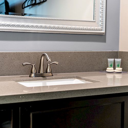 A bathroom countertop with a sink, faucet, mirror, toiletries, and a tissue box on it. There are shelves beneath the sink with towels.