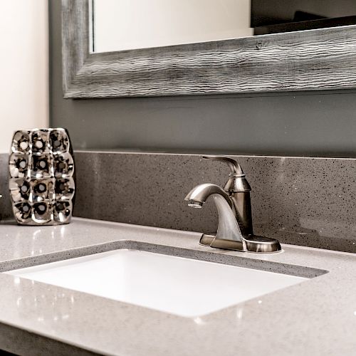 A modern bathroom sink with a silver faucet, a large framed mirror above it, and a soap dispenser on the countertop.