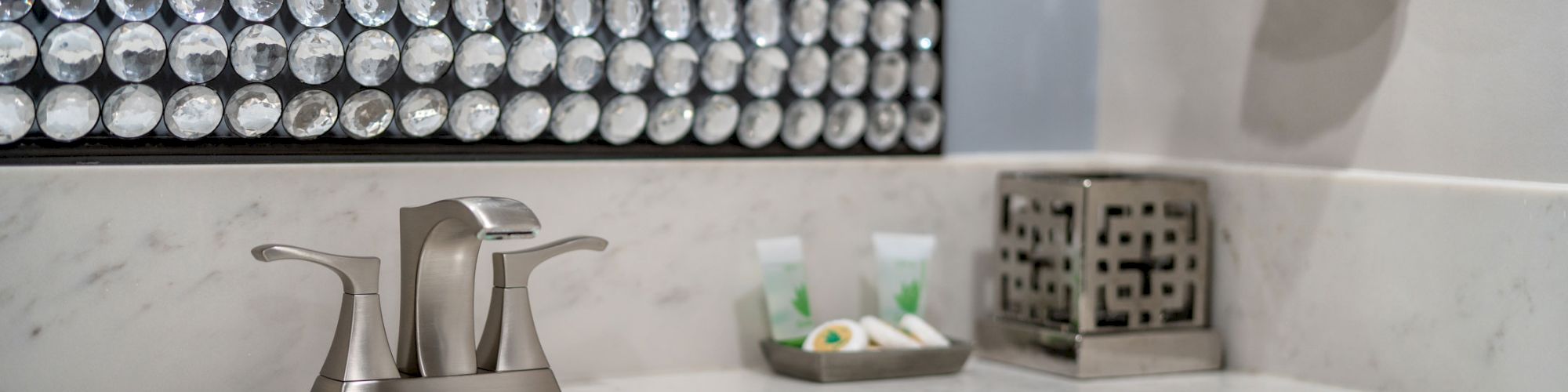 The image shows a bathroom sink with a marble countertop, a metallic faucet, decorative mirror, towel ring with a white towel, and a soap dish.