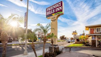 The image shows a street scene with a sign for "Friendly Hills Inn" against a bright, sunny sky and palm trees. The inn is located at 14329.