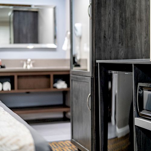 The image shows a modern hotel room with a microwave, mini fridge, and TV. A sink with a mirror and towels is visible in the background.