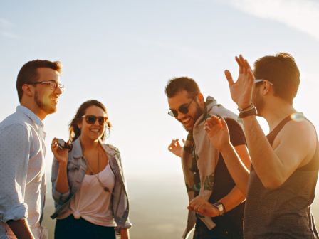 A group of four friends, two men and two women, are outdoors smiling and enjoying the sunshine, looking happy and relaxed together.